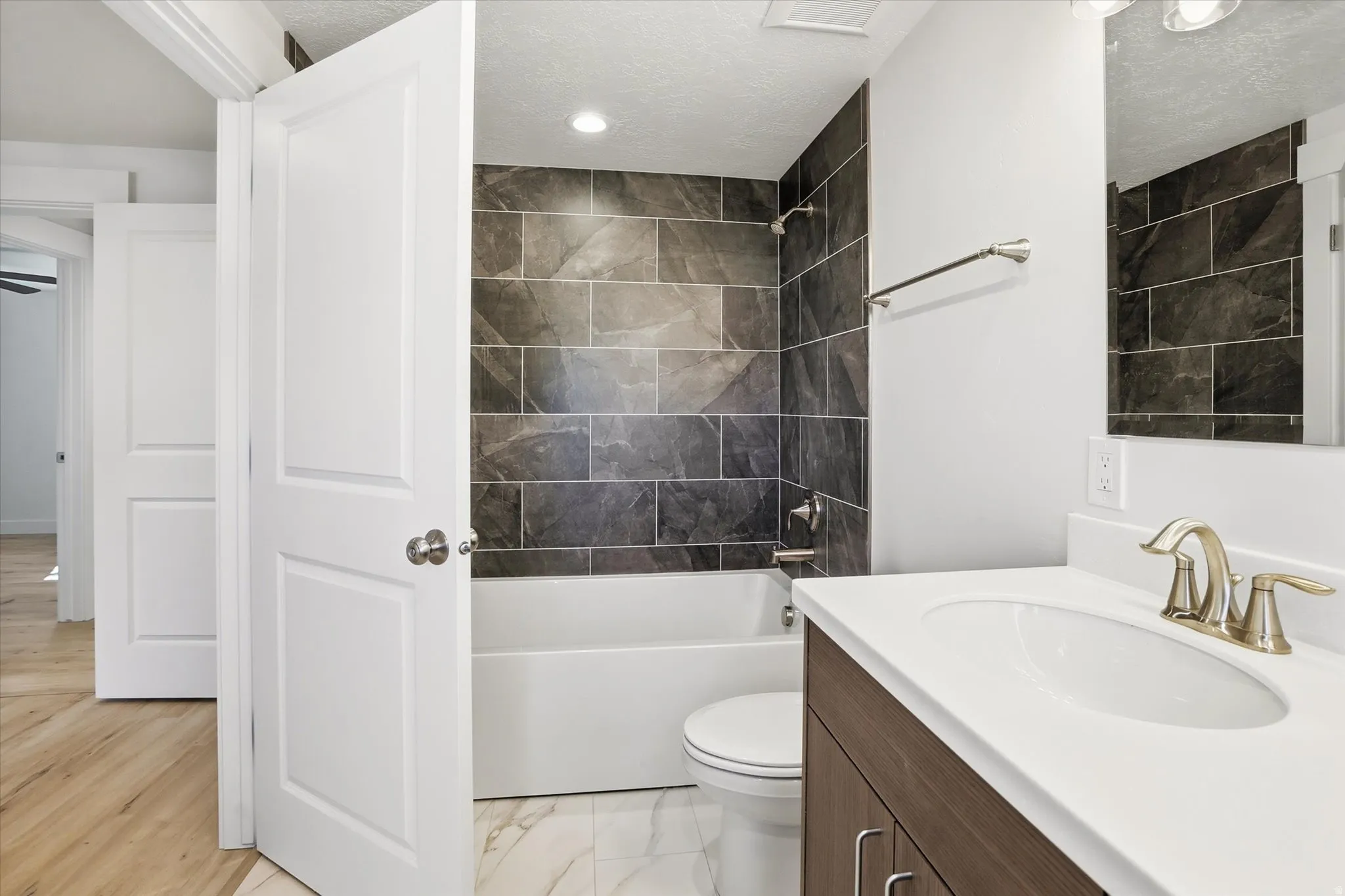Main Floor Hallway Bathroom featuring vanity, bathtub / shower combination, light marble finish floors, and a textured ceiling