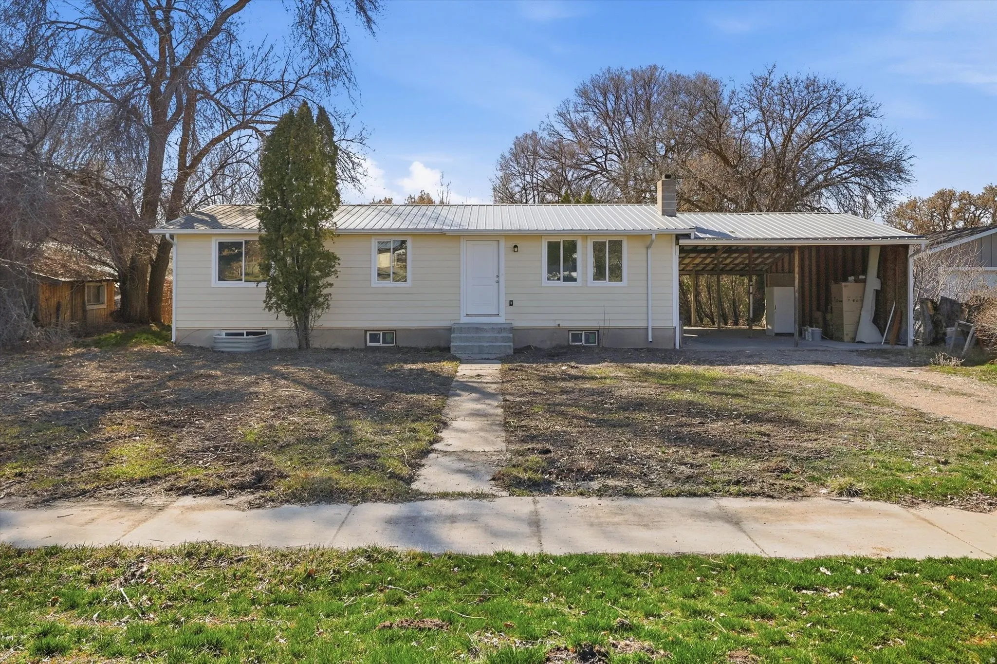 Single story home with a metal roof, a chimney, a carport, and driveway