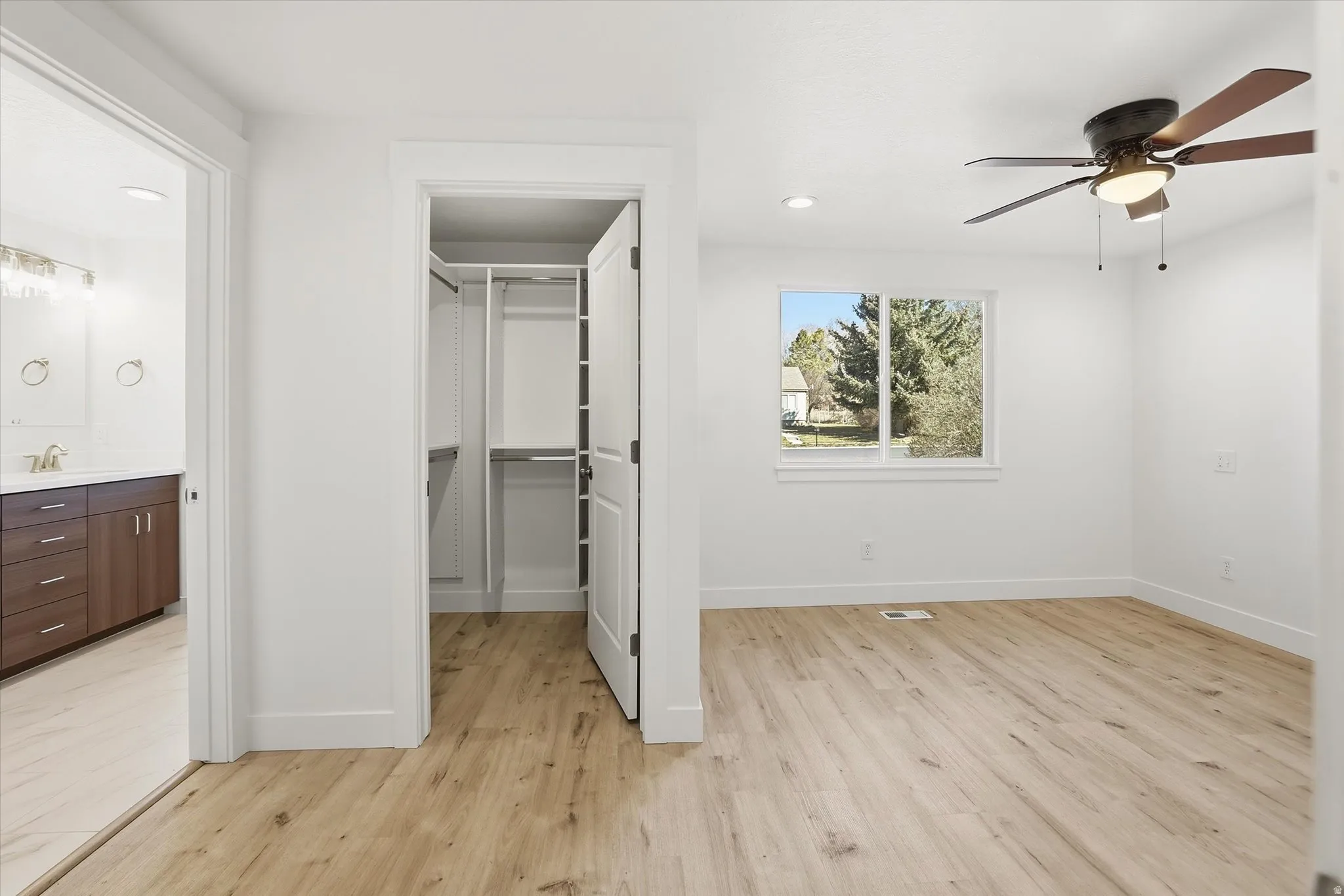 Primary Suite Unfurnished bedroom featuring ensuite bathroom, light wood-type flooring, a spacious closet, recessed lighting, and a ceiling fan