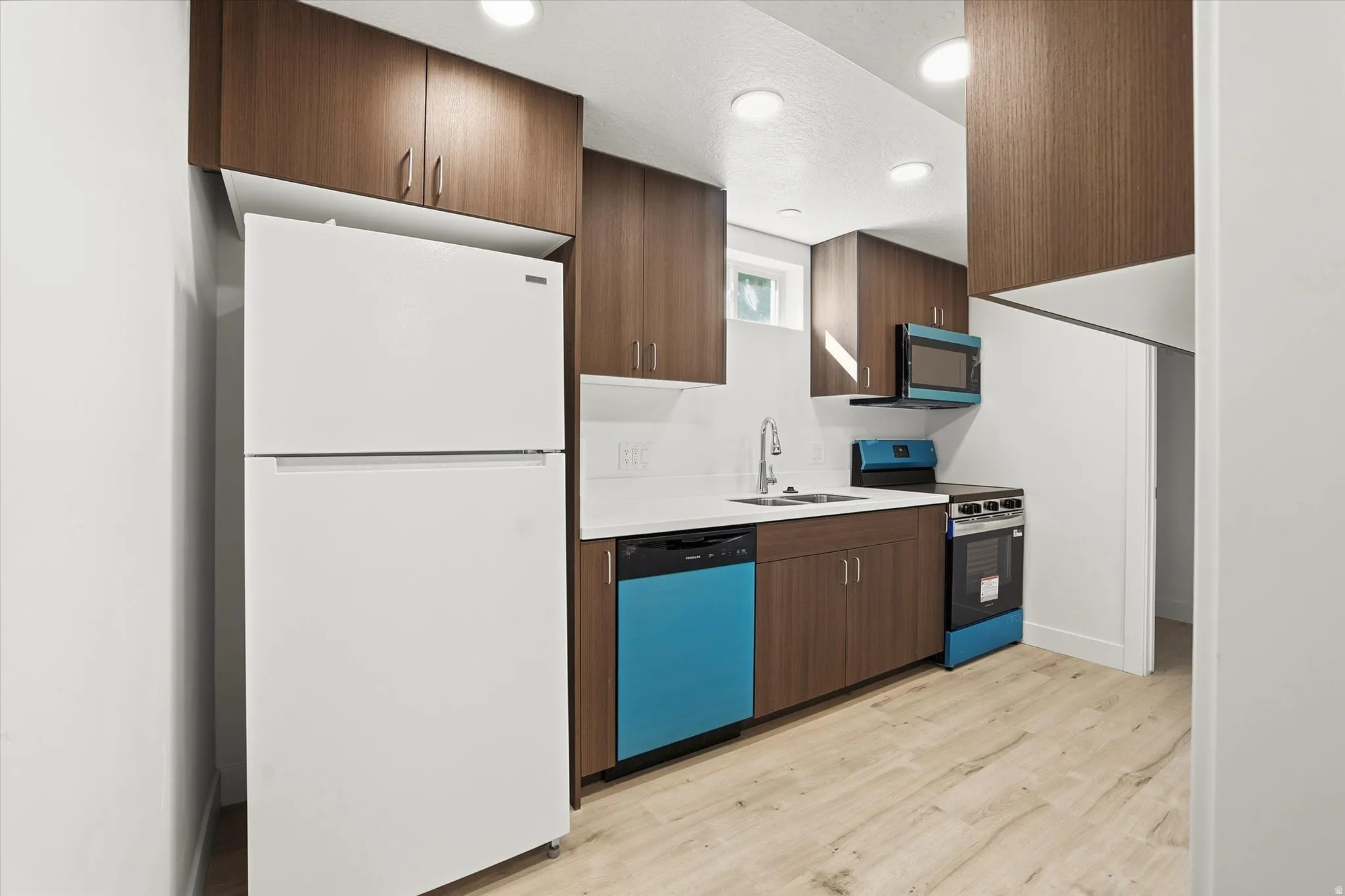 Kitchen with freestanding refrigerator, stainless steel electric stove, light countertops, dishwasher, and light wood-style flooring