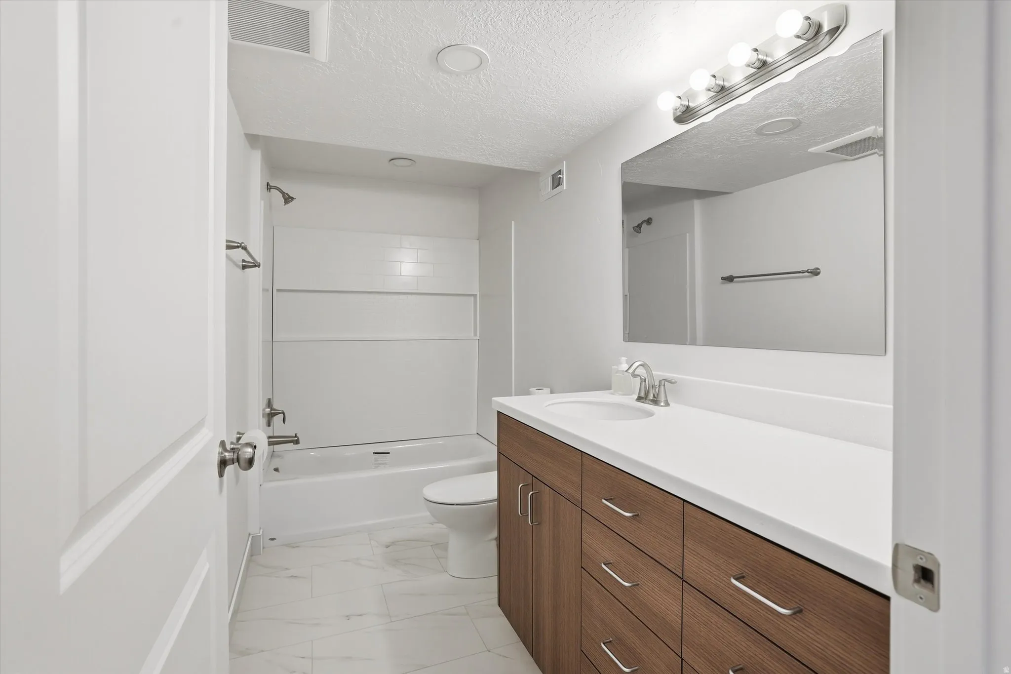 Basement Bathroom featuring vanity, shower / washtub combination, a textured ceiling, and light marble finish flooring