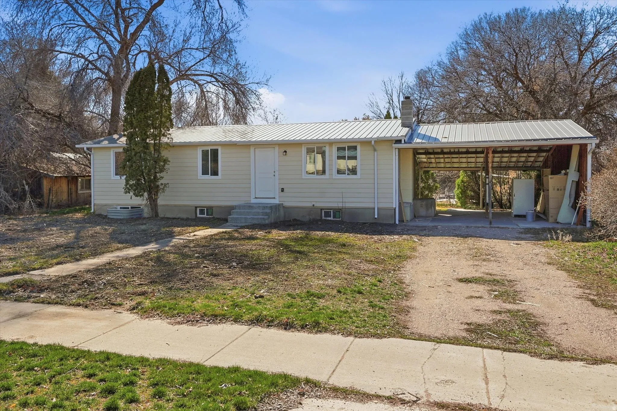 Ranch-style home with a metal roof, a chimney, dirt driveway, and a carport
