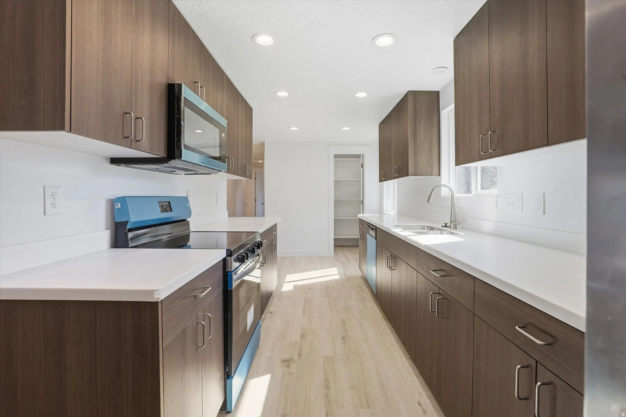 Kitchen featuring stainless steel appliances, modern cabinets, light wood finished floors, recessed lighting, and dark wood finish cabinetry