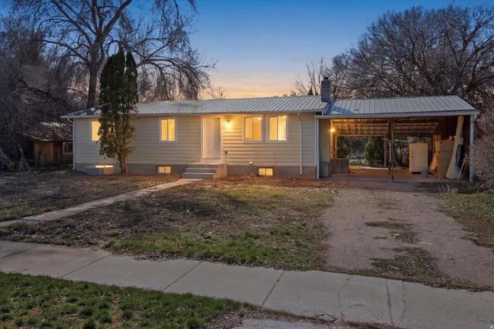 View of front of home featuring a metal roof, dirt driveway, a chimney, and an attached carport