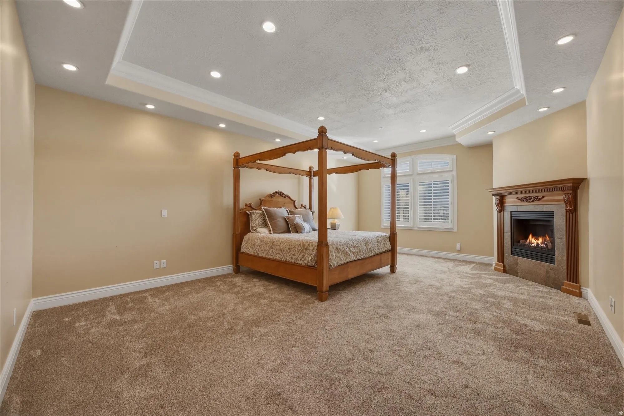Bedroom featuring a raised ceiling, crown molding, light colored carpet, a fireplace, and recessed lighting