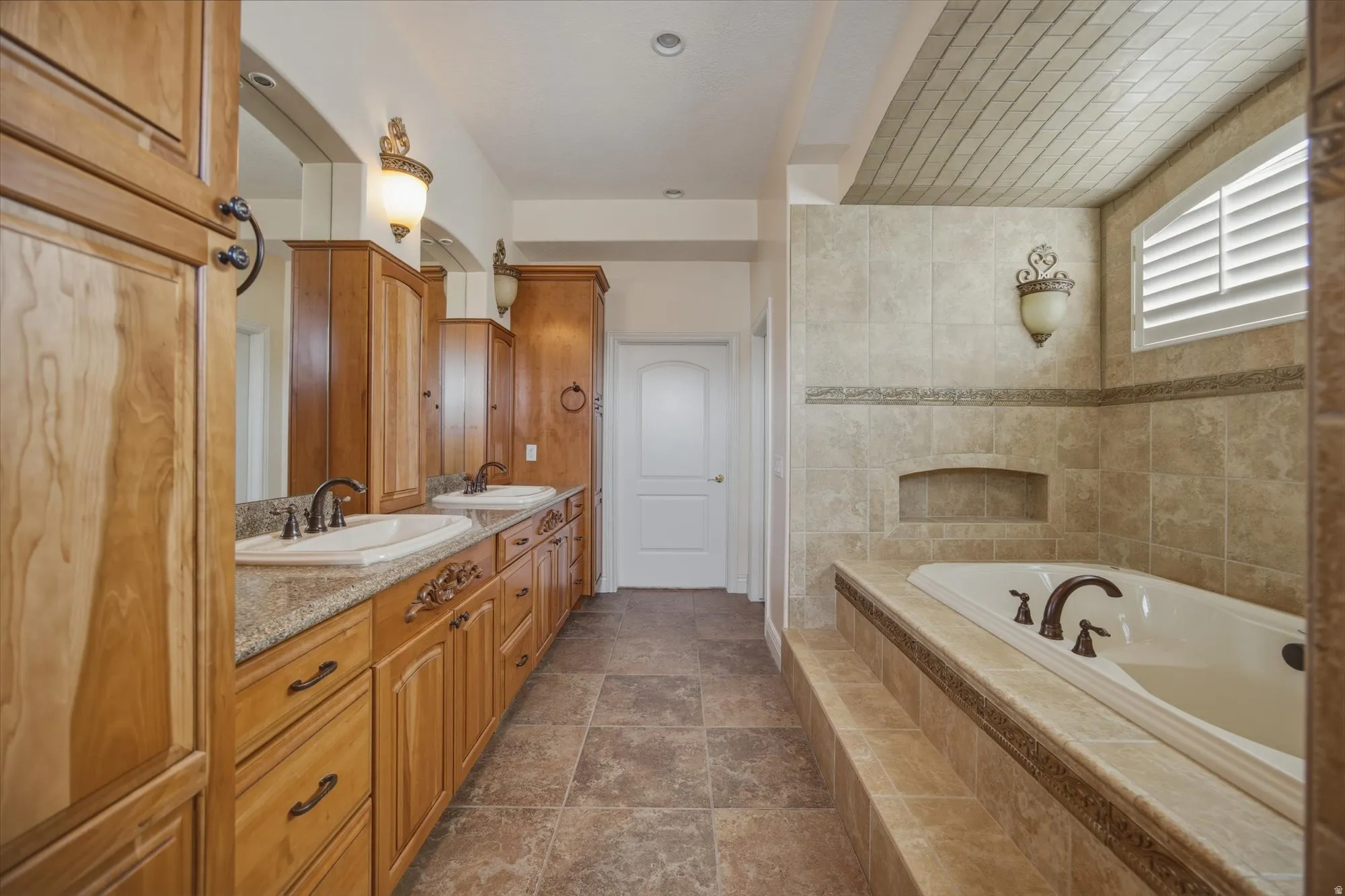 Full bathroom with double vanity, a bath, and dark stone finish floors