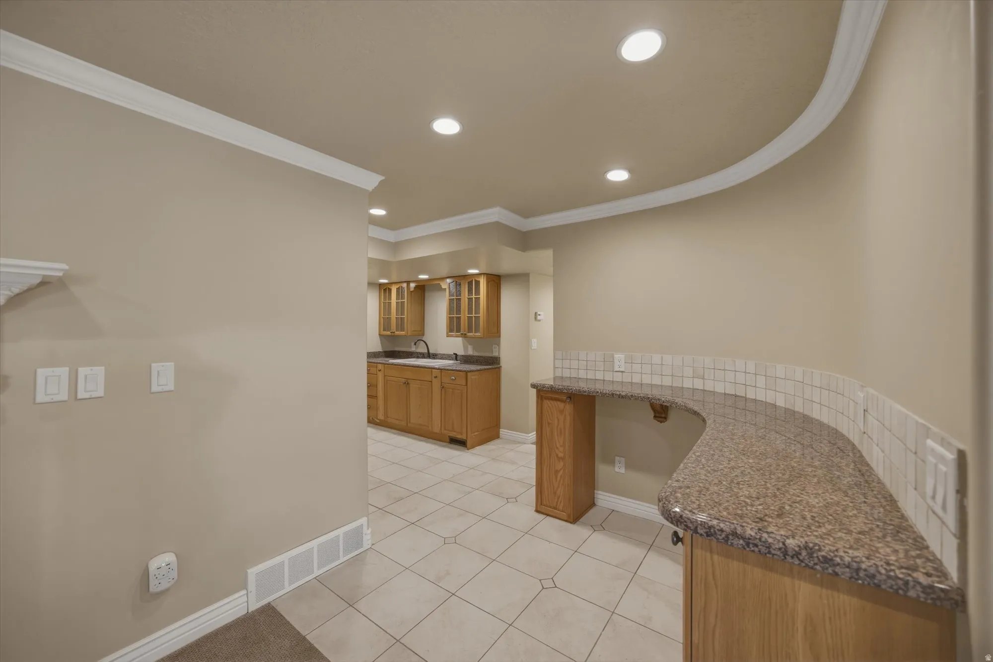 Kitchen featuring glass insert cabinets, wood finish cabinets, ornamental molding, recessed lighting, and light tile patterned floors