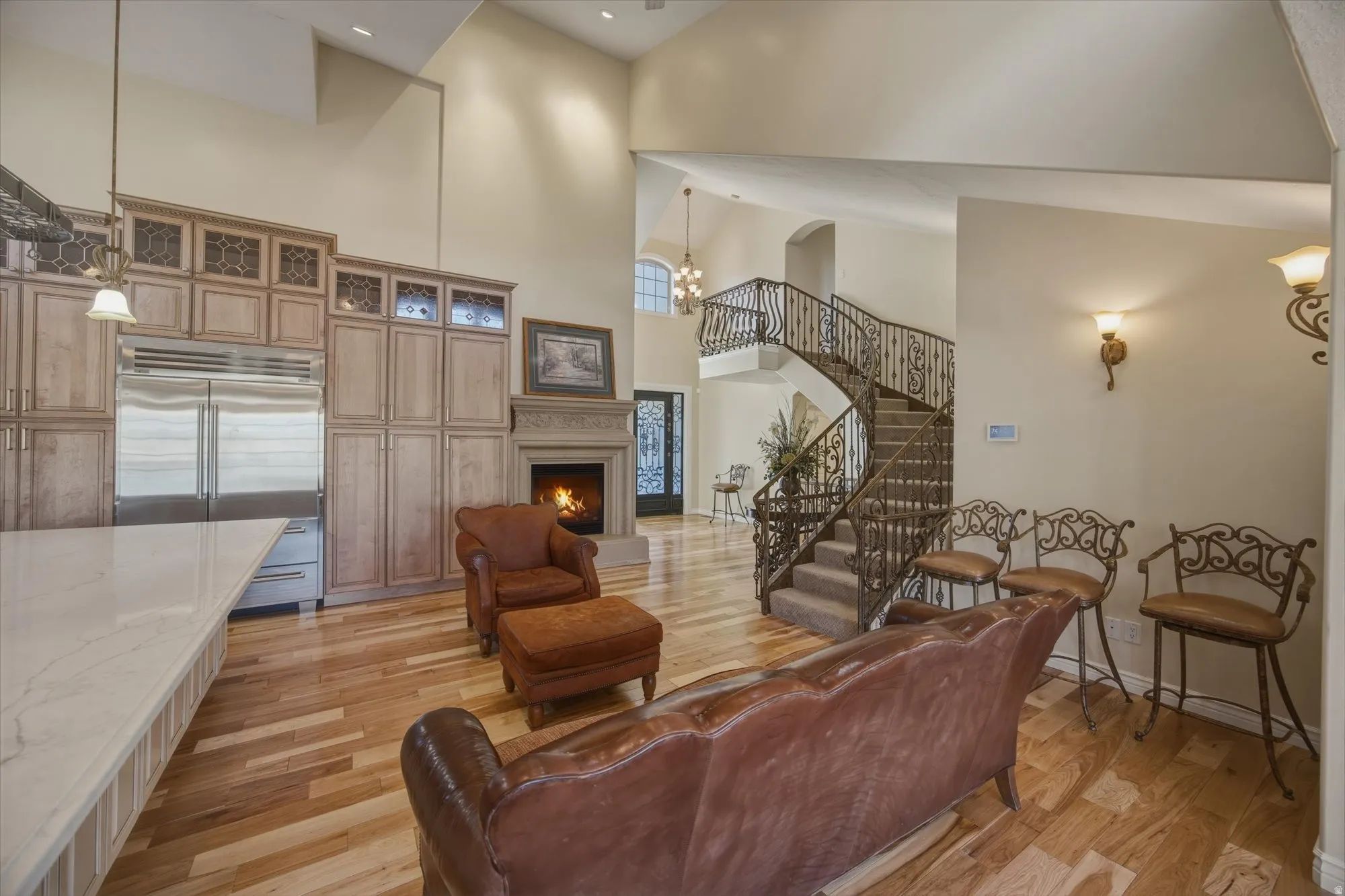 Living room featuring light wood-type flooring, a lit fireplace, suspended lighting, and a high ceiling