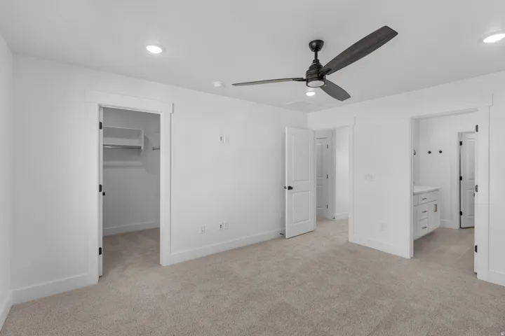 Unfurnished bedroom with a spacious closet, light carpet, ensuite bathroom, ceiling fan, and recessed lighting