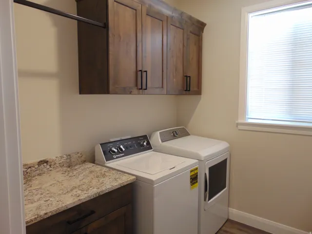Laundry room featuring wood-finish cabinetry with black hardware, a light-toned countertop, and a window with blinds