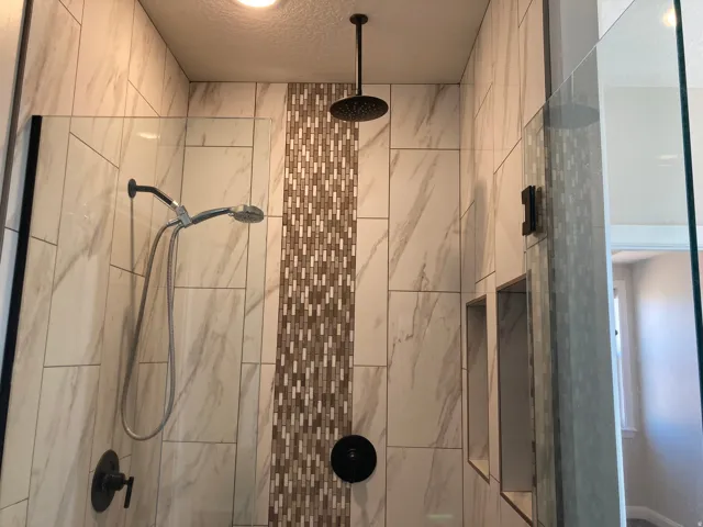 Tiled shower enclosure featuring a rain shower head, handheld shower, built-in niches, and a decorative mosaic tile accent