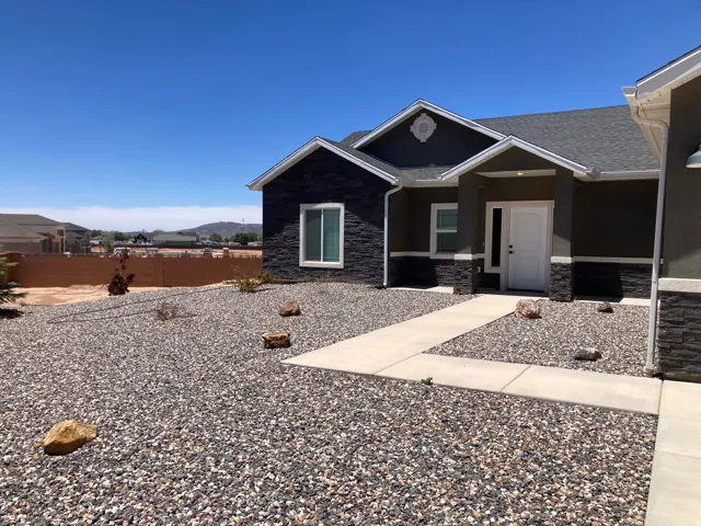 Contemporary exterior featuring dark gray stucco siding with black stacked stone accents and a white entry door