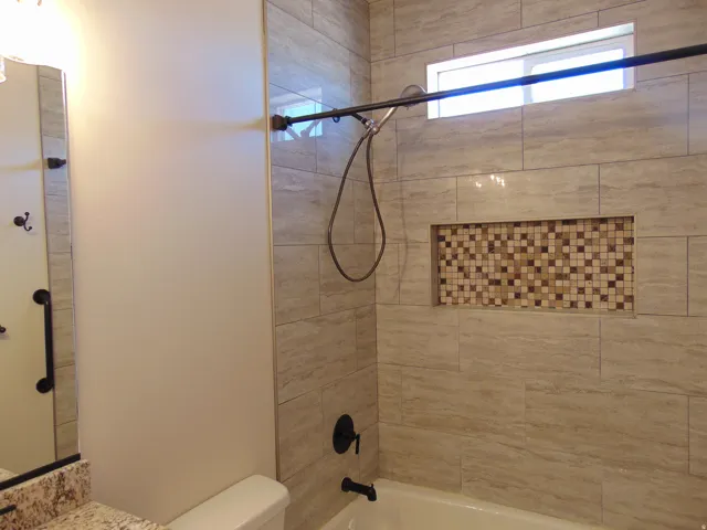 Tiled shower surround with an accent mosaic niche, finished with a dark bronze shower fixture and a high transom window