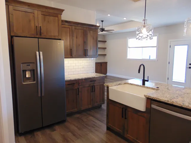 Kitchen featuring a farmhouse sink, stainless steel appliances, granite countertops, wood-finish flooring, and white subway tile backsplash