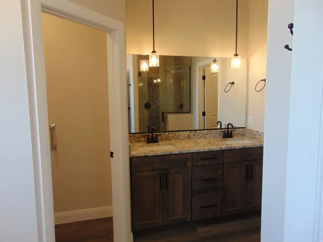 Bathroom vanity featuring a dual sink design, granite countertop, rich wood-finish cabinetry, and contemporary pendant lighting