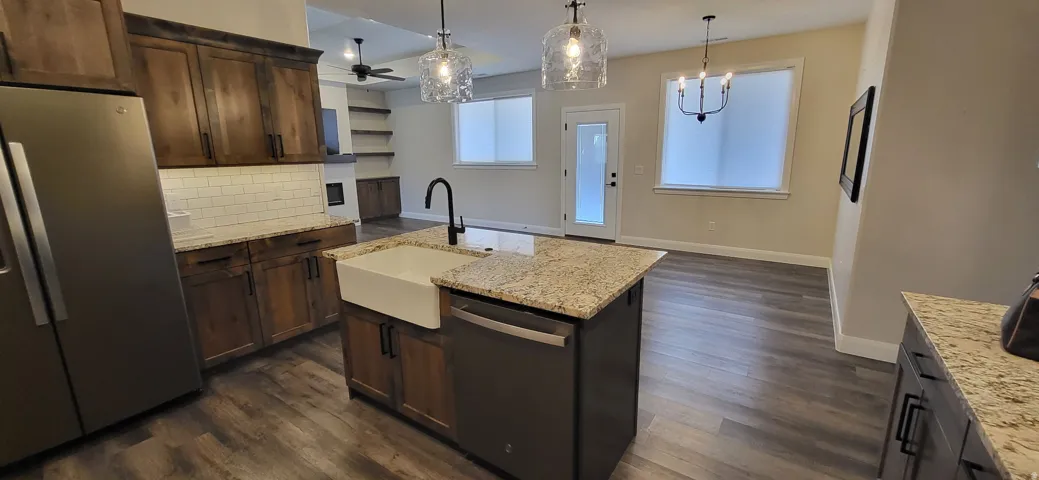 Wood-finish flooring, granite countertops, an undermount farmhouse sink, recessed lighting, and a kitchen island with built-in appliances