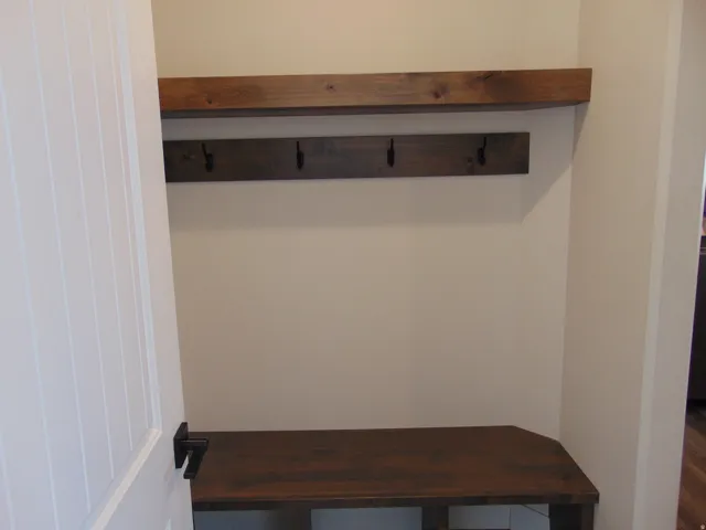 Built-in wood-finish bench with overhead shelf and wall-mounted coat hooks