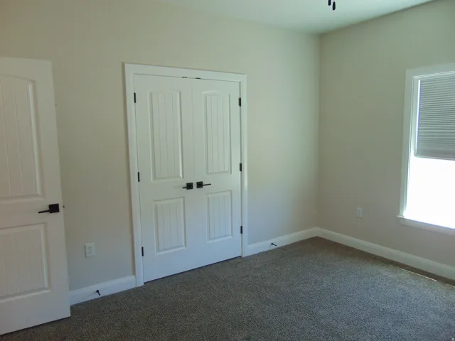 Carpeted room featuring a double bifold door, white trim, neutral wall paint, and a window with blinds