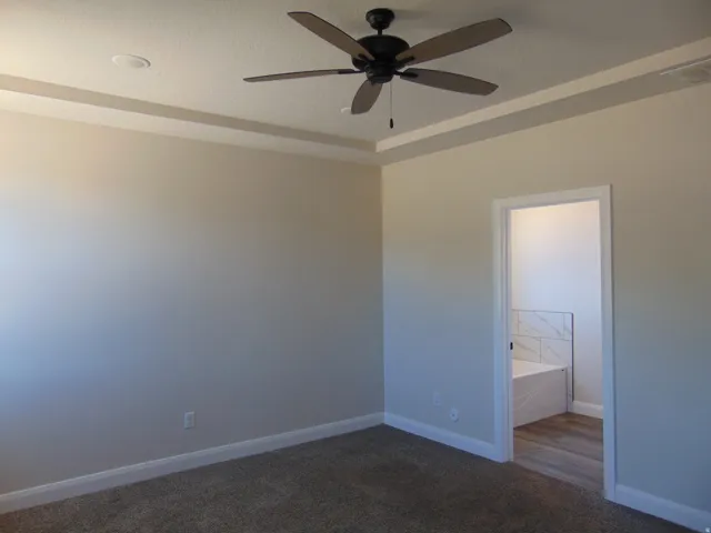 Neutral-toned room featuring a tray ceiling with recessed lighting and a ceiling fan