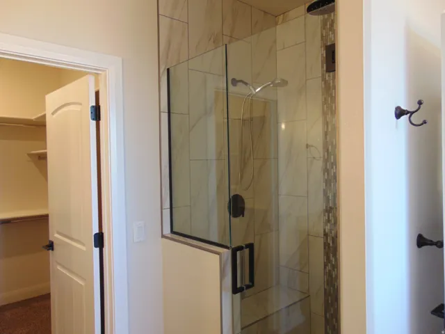 Contemporary glass-enclosed shower featuring a tiled surround with a decorative mosaic accent, a built-in bench, and a rain shower head