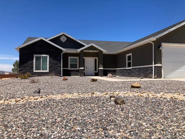 Contemporary single-story residence featuring a dark gray stucco exterior with dark stacked stone accents