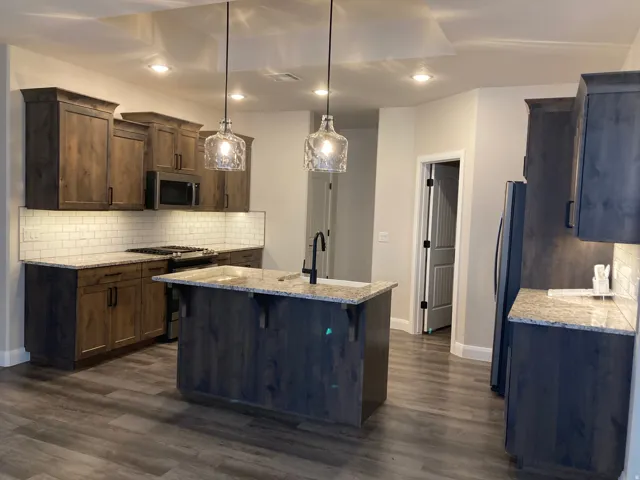 Kitchen featuring wood-finish cabinetry, light-toned countertops, subway tile backsplash, and wood-finish flooring