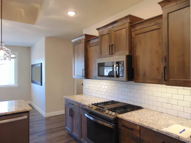 Kitchen featuring wood-finish cabinetry with crown molding, stainless steel appliances, granite countertops, and a subway tile backsplash