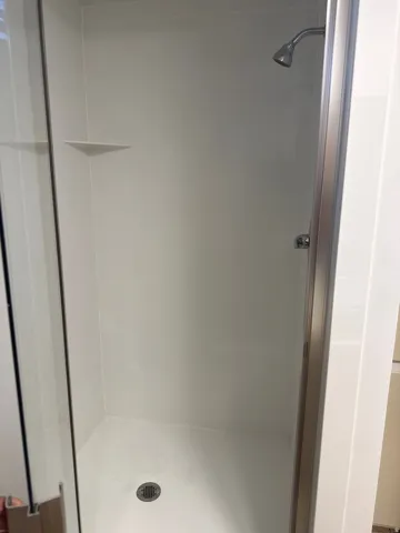 Enclosed shower with a bright white surround, integrated corner shelving, and a chrome showerhead