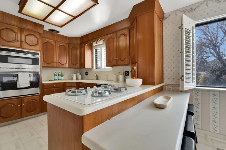 Kitchen featuring wood finish cabinetry, light countertops, a kitchen bar, stainless steel double oven, and light floors