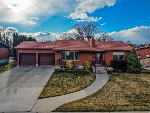 Ranch-style home with an attached garage, brick siding, a tiled roof, and driveway