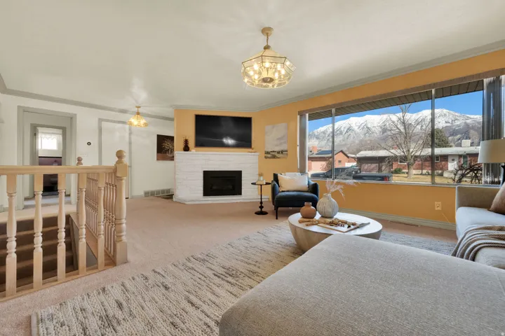 Carpeted living room featuring suspended lighting, a fireplace, and ornamental molding