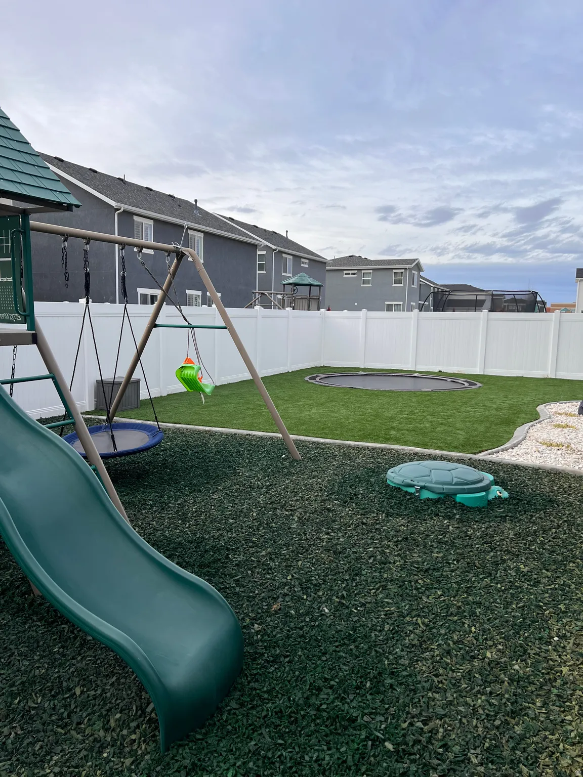 Fenced backyard featuring a playground and a trampoline