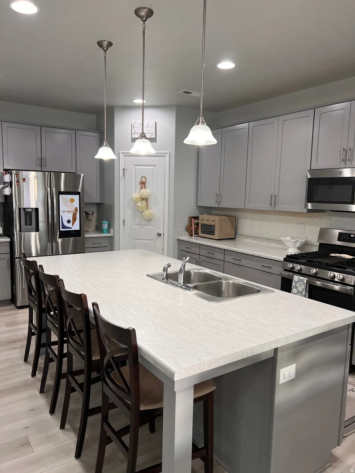 Kitchen with gray cabinets, a kitchen breakfast bar, light countertops, and a kitchen island with sink