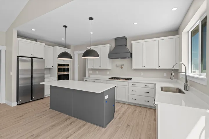 Kitchen featuring stainless steel appliances, light stone counters, two tone cabinetry, light wood-type flooring, and a center island