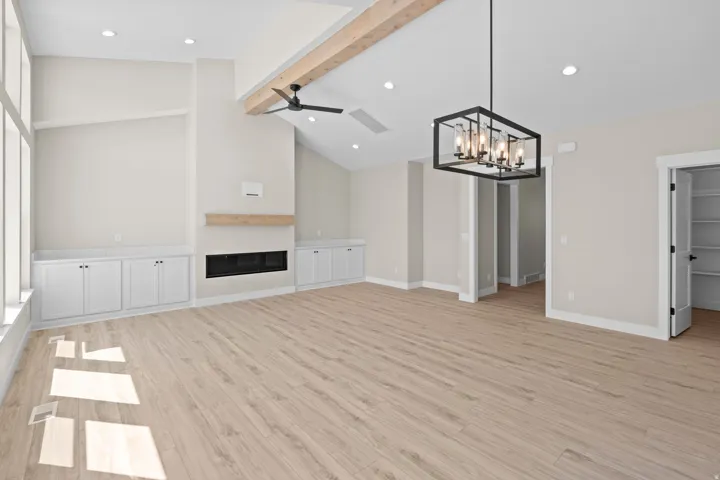 Unfurnished living room with a glass covered fireplace, light wood finished floors, vaulted ceiling with beams, a ceiling fan, and hanging lights