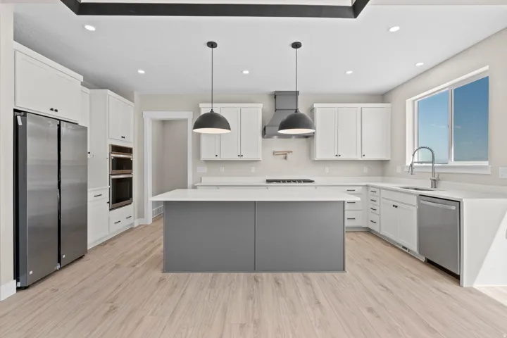 Two tone kitchen featuring stainless steel appliances, two tone color scheme, light stone counters, a center island, and hanging light fixtures