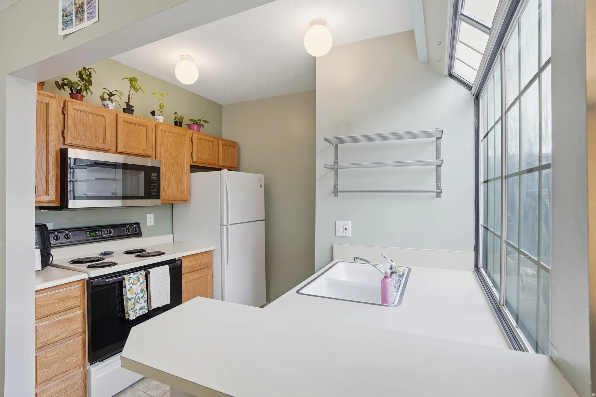 Kitchen featuring range with electric stovetop, light countertops, stainless steel microwave, freestanding refrigerator, and a peninsula