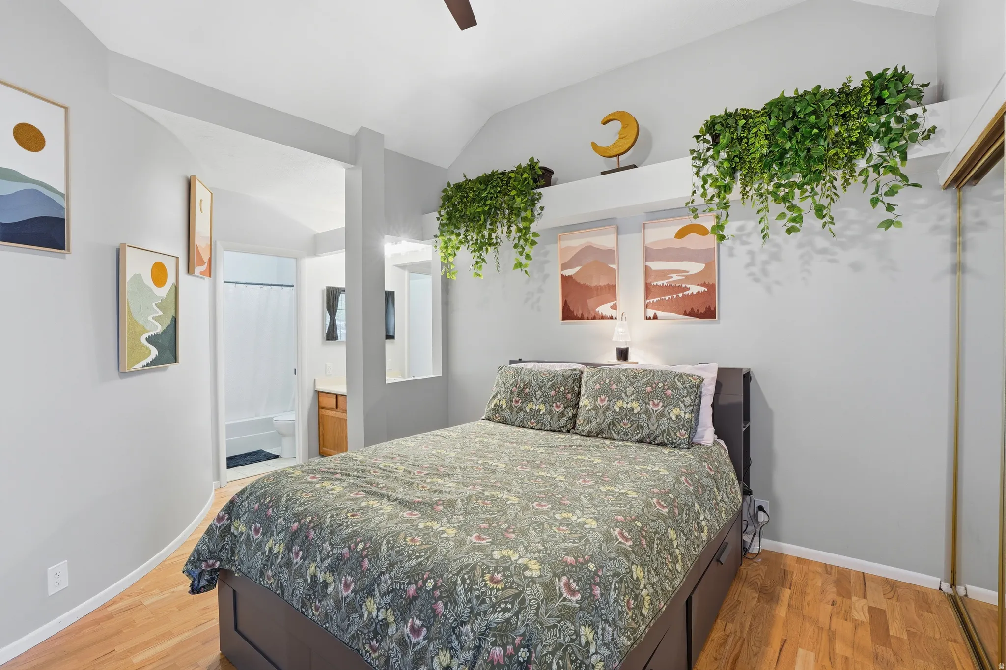 Bedroom with vaulted ceiling, light wood-type flooring, ensuite bath, a ceiling fan, and a closet