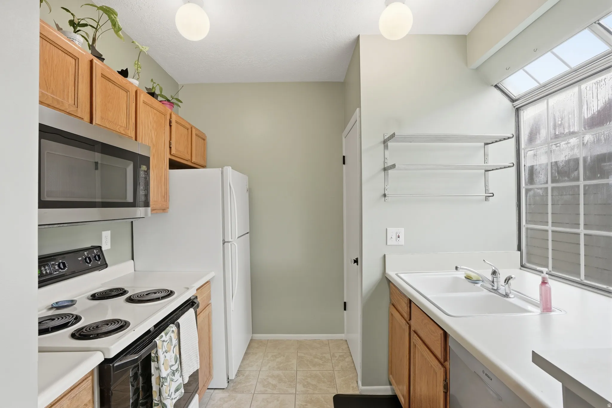 Kitchen featuring black electric range oven, stainless steel microwave, light countertops, and dishwashing machine