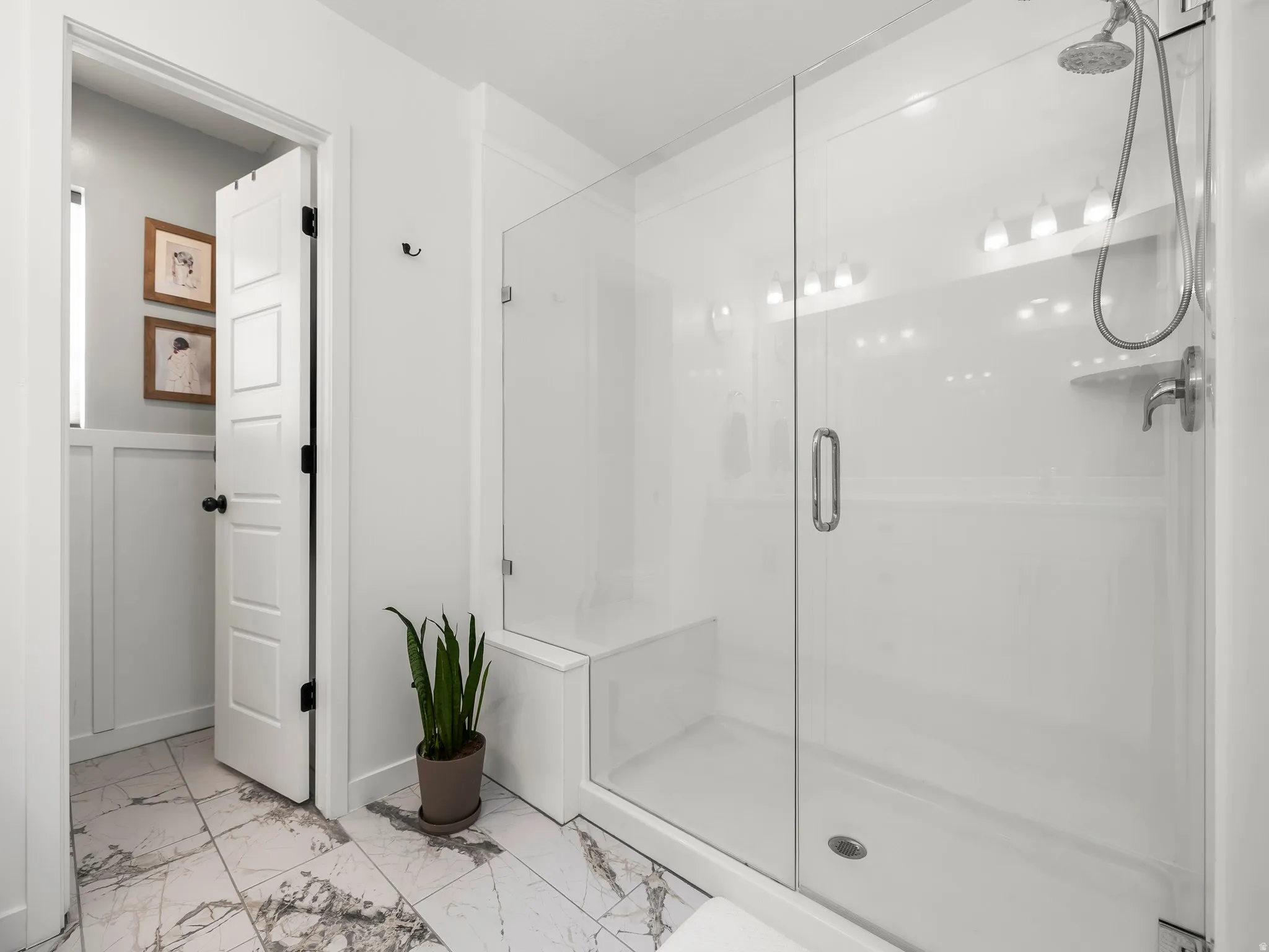 Full bath featuring a shower stall, light marble finish flooring, and wainscoting