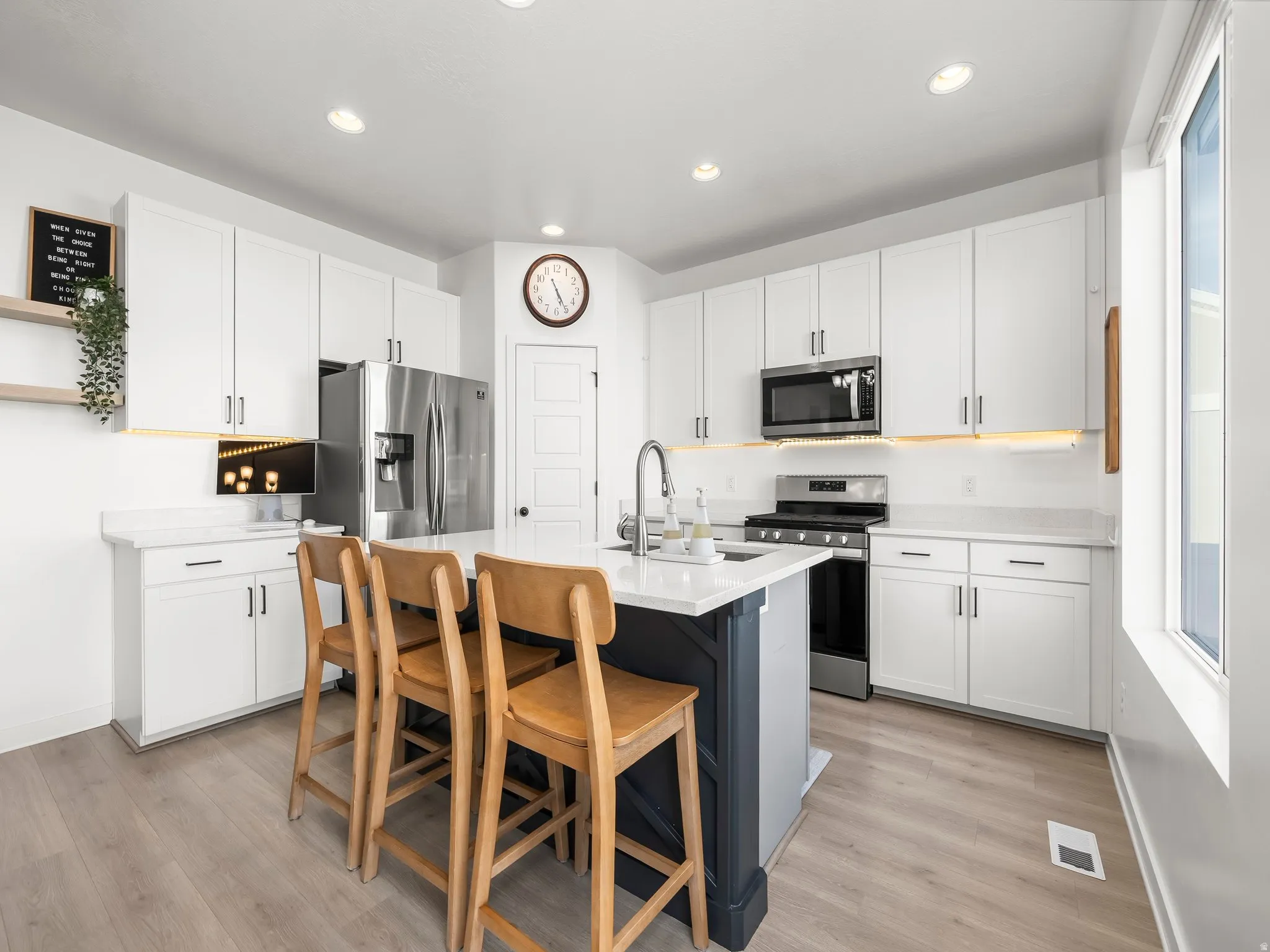 Kitchen with stainless steel appliances, light wood-style floors, a breakfast bar area, an island with sink, and two tone color scheme
