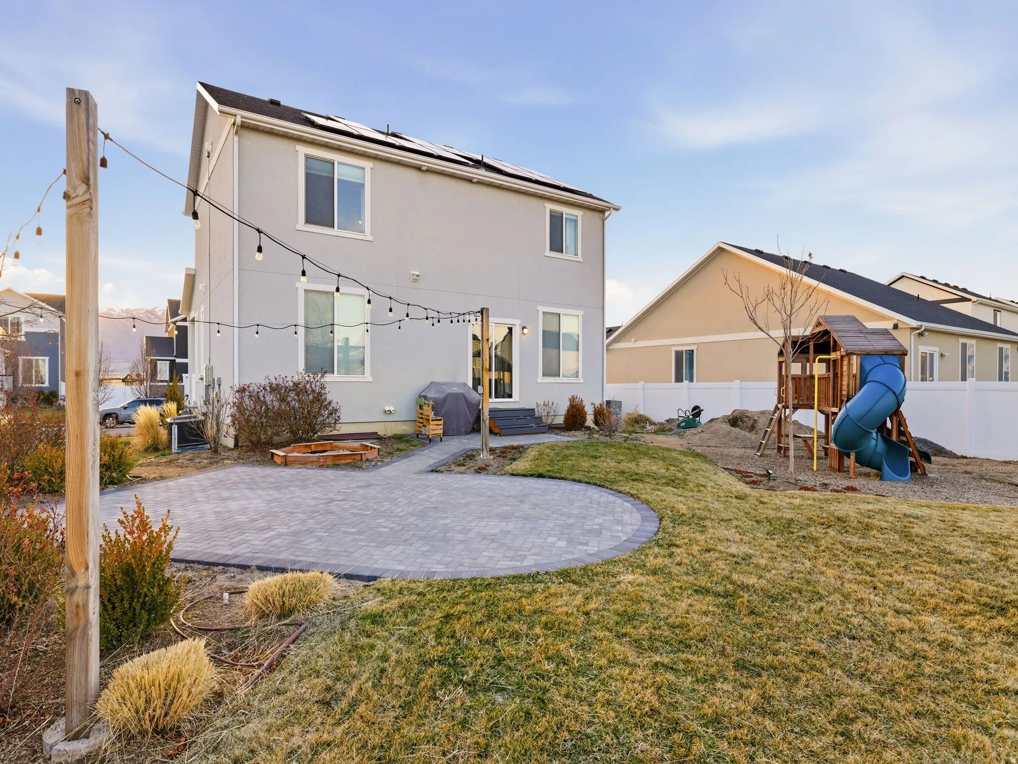 Rear view of property featuring a patio area, a playground, solar panels, a fenced backyard, and stucco siding