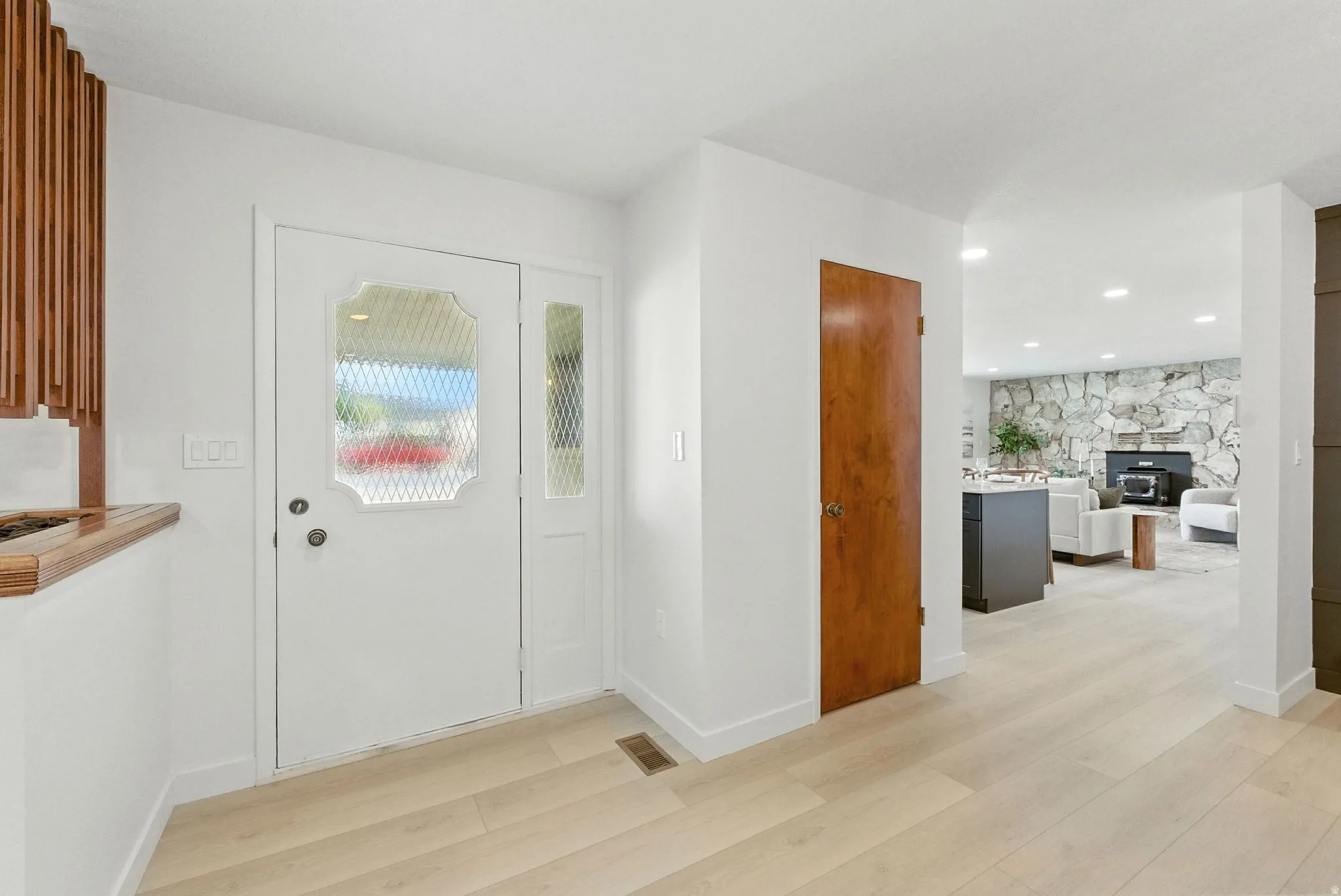Entrance foyer featuring light wood finished floors, a stone fireplace, and recessed lighting