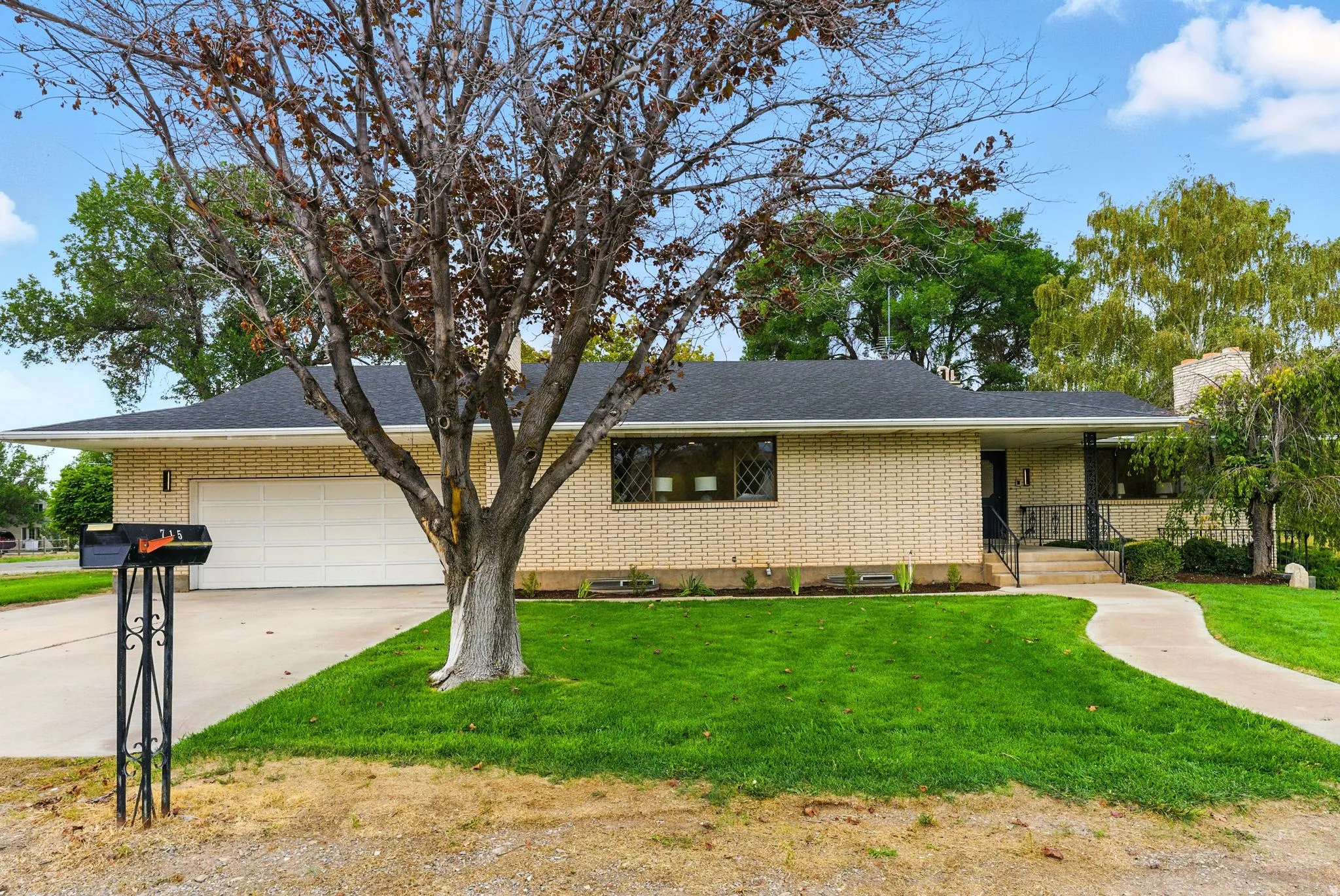 Ranch-style home featuring brick siding, an attached garage, a front lawn, driveway, and covered porch
