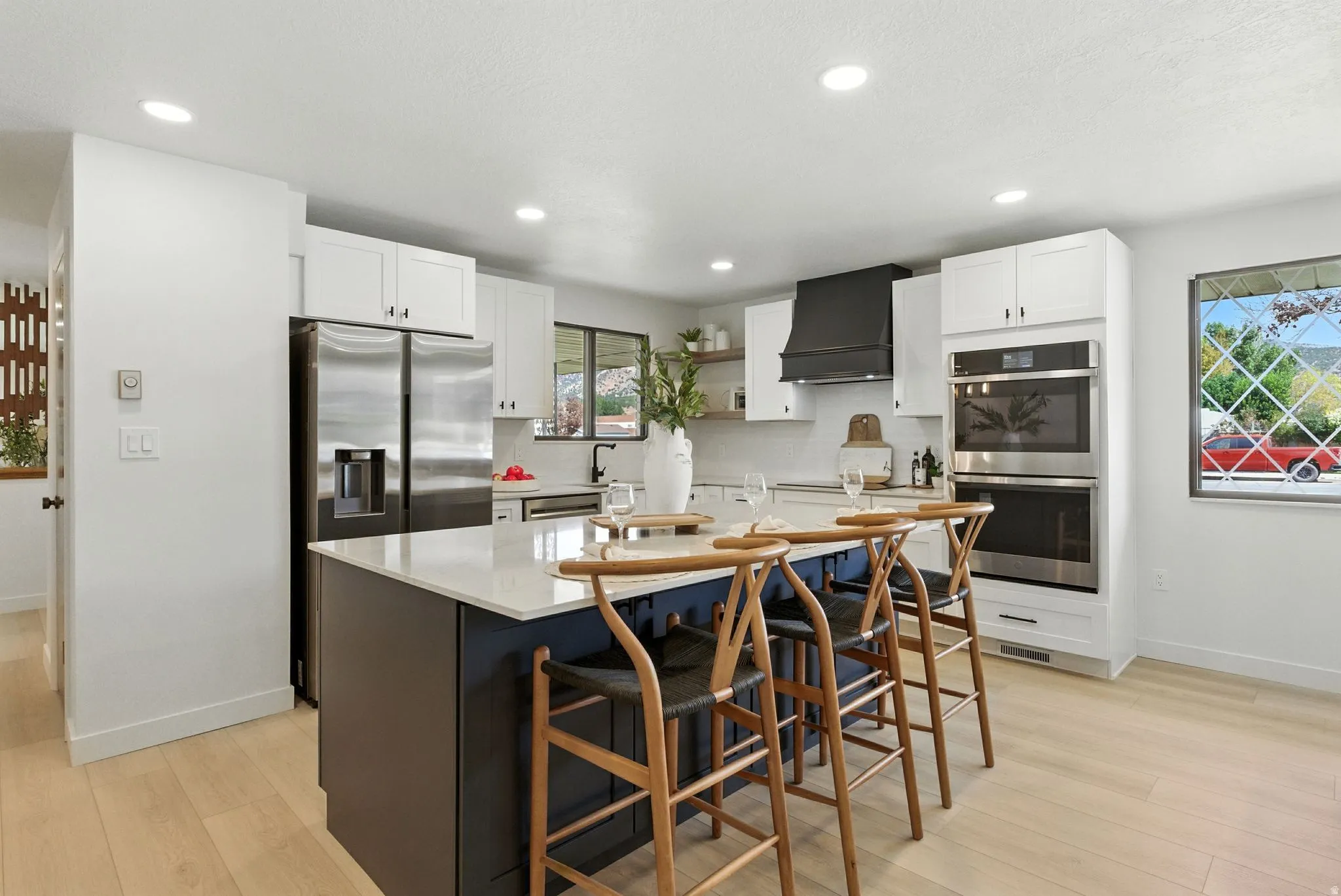 Dual tone kitchen with stainless steel appliances, a kitchen island with sink, light wood finished floors, light stone countertops, and dual tone cabinetry