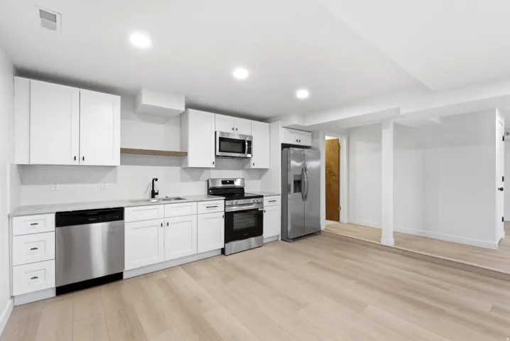 Modern kitchen featuring white cabinetry, stainless steel appliances, light wood-finish flooring, and recessed lighting