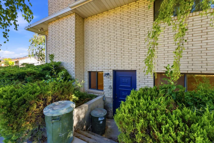 Brick exterior with a vibrant blue entry door, complemented by mature green landscaping and a small window