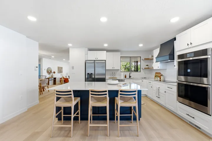 Spacious kitchen featuring a large central island with seating, stainless steel appliances, white cabinetry, and wood-finish flooring