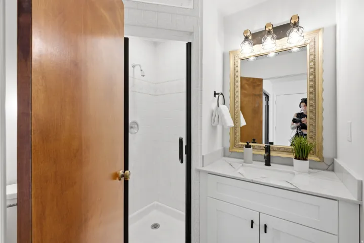 Bathroom featuring a white vanity with a marble-finish countertop, a decorative gold-toned framed mirror, and a frameless glass shower enclosure with white subway tile