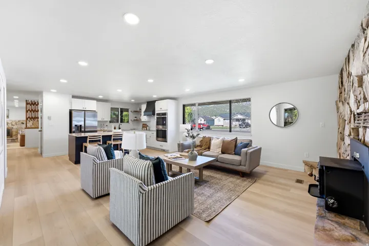 Open-concept living area featuring light wood-finish flooring, recessed lighting, a stone accent wall, and expansive windows
